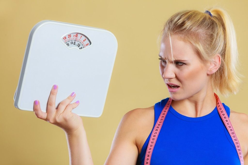 Fit fitness woman with scale. Frustrated angry blonde girl holding weight scales. Time for slimming weightloss diet and healthy lifestyles concept