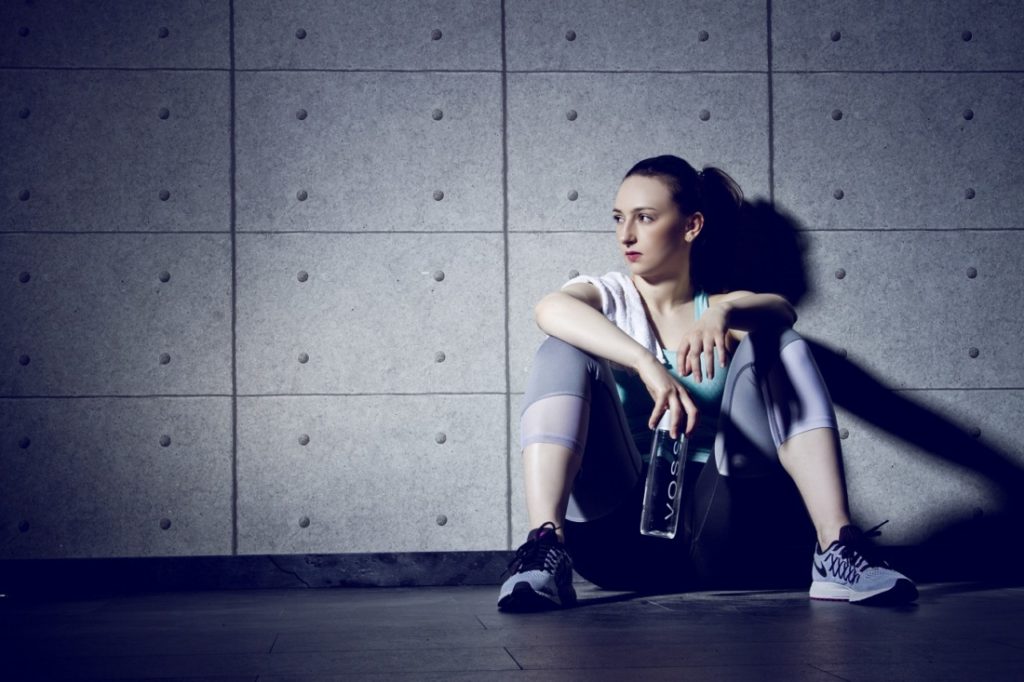 Young woman in sports clothes sitting on the ground after an intense EMOM workout.