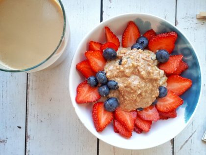 Oatmeal topped with strawberries, blueberries, honey and crunchy peanut butter next to a cup of coffee.
