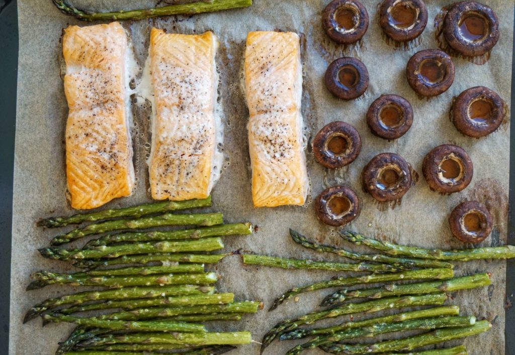 Baked salmon, asparagus and mushrooms on a baking tray.