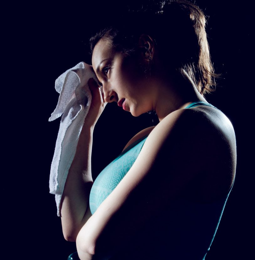 Fit girl wiping her sweat from her forehead with a towel.