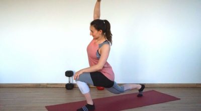 Young woman in sports outfit performing forward lunge with psoas reach on a yoga mat.