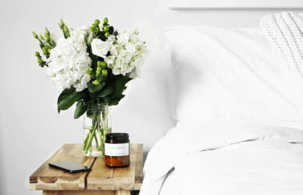 a beautiful bedside table with flowers and a candle from the article "how to improve sleep with anxiety"