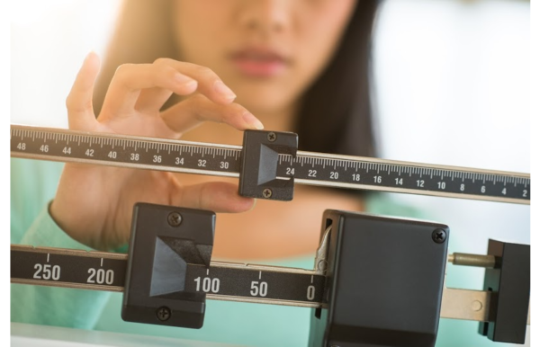 A woman weighing herself to check her weight loss progress from the article "10 Worst weight loss myths delaying your success"